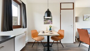 Uma sala de jantar com uma mesa, duas cadeiras, uma luminária pendente, um quadro e um radiador.