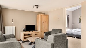Ett modernt hotellrum med en grå soffgrupp, ett träskåp, en tv och en säng med vita sängkläder.