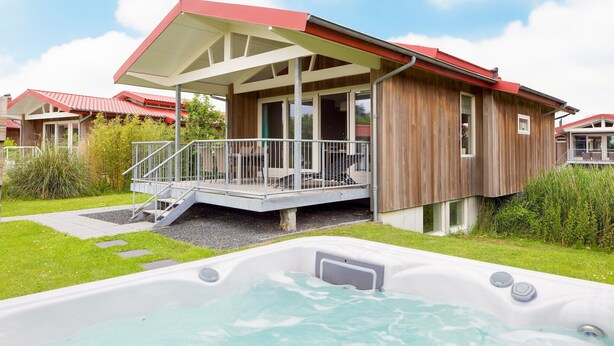 Une cabane en bois avec un balcon, un jacuzzi et une cour gazonnée.