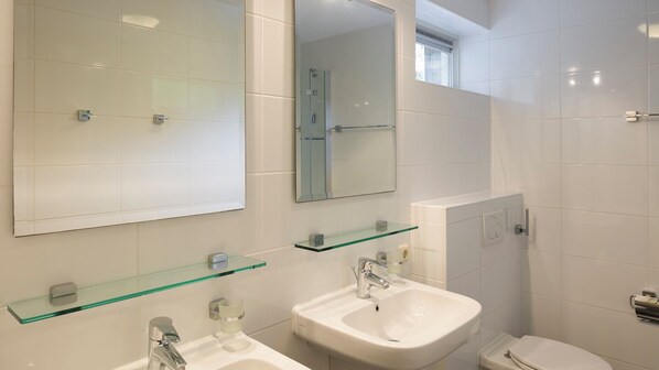 A modern bathroom with two sinks, a glass shelf, a mirror, and a toilet.