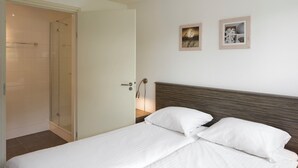 Une chambre d’hôtel avec un lit, une table de chevet, une lampe fixée au mur et deux tableaux encadrés.