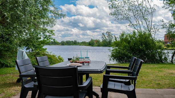 An outdoor table with chairs, a tablecloth, and a view of a lake. - Detached bungalow for 9 persons (Vlagtwedde)