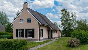 A two-story house with a sloped roof, a chimney, and a small porch. - Detached bungalow for 9 persons (Vlagtwedde)