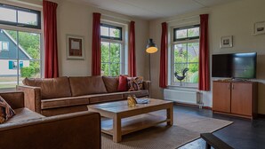 A living room with a brown sofa, a wooden coffee table, and a television on a cabinet. - Detached bungalow for 9 persons (Vlagtwedde)