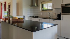 A modern kitchen with a large island, white cabinetry, a stainless steel countertop, and a window above the sink. - Detached bungalow for 9 persons (Vlagtwedde)