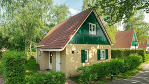 A small, single-story house with a sloped roof, green exterior walls, and a brick foundation. - Comfortable bungalow for 4 persons (Diessen-Baarschot)