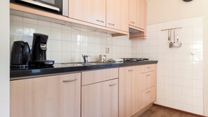 A kitchen with light wood cabinets, a black countertop, a coffee maker, and a stove. - Comfortable bungalow for 4 persons (Diessen-Baarschot)