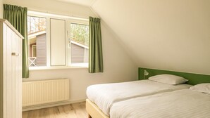 A bedroom with two beds, a window with curtains, a radiator, and a green headboard. - Detached bungalow for 14 persons (Vlagtwedde)