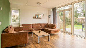 A modern living room with a brown leather sectional sofa, a wooden coffee table, and a large sliding glass door leading to an outdoor area. - Detached bungalow for 14 persons (Vlagtwedde)