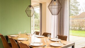 A dining area with a wooden table set for six, two pendant lights, and a view of the garden through large windows. - Detached bungalow for 14 persons (Vlagtwedde)