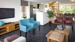 A modern living room with a flat-screen TV, a blue sofa, a wooden coffee table, and a dining area with brown leather chairs.