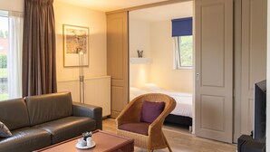 Een hotelkamer met een leren bank, een rieten stoel en een bed met een blauw zonnescherm.