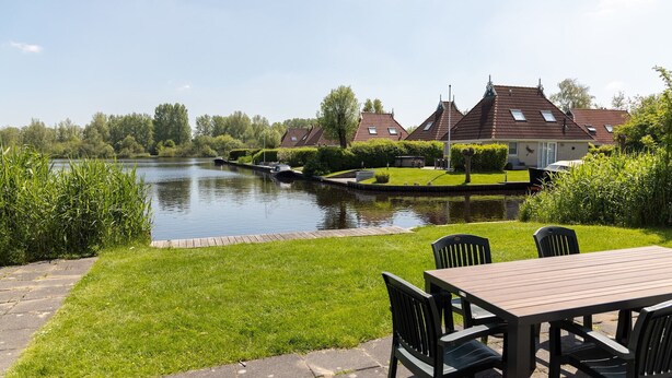 Een pand aan de rivier met een houten terras en stoelen, een kanaal en traditionele huizen met rode daken.