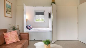 Habitación compacta con cama integrada, una ventana pequeña, televisión y planta sobre una mesa.