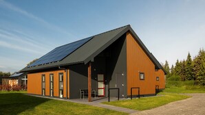 A modern building with a sloped roof, large windows, and a door with a red frame. - Detached villa for 6 persons (Tynaarlo)