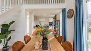 A dining area with a wooden table, chairs, a vase with flowers, and a staircase leading to an upper level. - Detached villa for 6 persons (Tynaarlo)