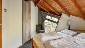 Una camera da letto con soffitto in legno, un letto con biancheria bianca, una sedia e una finestra vista verde.