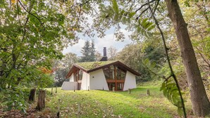 Una piccola casa di legno bianca con tetto spiovente, circondata da alberi e da un'area verde.