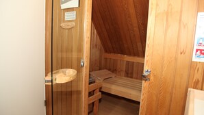 A wooden sauna room with a wooden bench, a wooden toilet seat, and a wooden bench with a towel.