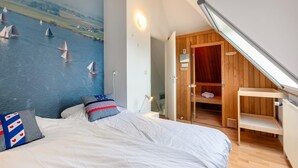 A bedroom with a large bed, a mural of sailboats on the wall, a wooden closet, and a skylight.