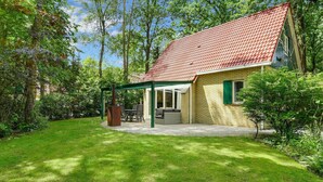A house with a red-tiled roof, a covered patio with a table and chairs, and a green lawn. - Luxury bungalow for 4 people (Diessen-Baarschot)