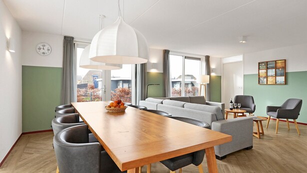 Un salon moderne avec une table à manger en bois, des canapés gris et une grande fenêtre donnant sur l’extérieur.