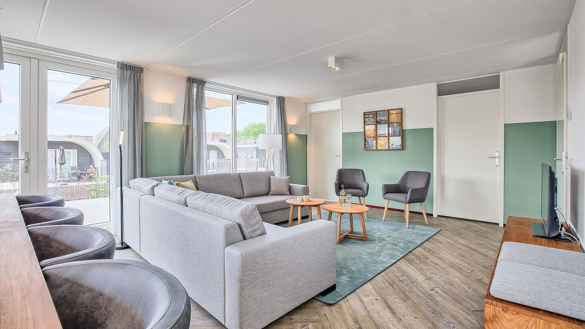 A modern living room with a grey sectional sofa, two armchairs, a small coffee table, and a TV.