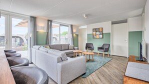 Un salon moderne avec un canapé d’angle gris, deux fauteuils, une petite table basse et un téléviseur.