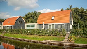 Une rangée de maisons modernes à deux étages, avec des toits orange, située au bord d’un canal.