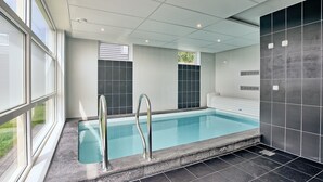 Une piscine intérieure moderne avec des parois en verre transparent, un sol carrelé et un plafond doté d’un éclairage encastré.
