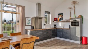 Eine moderne Küche mit Essbereich, inklusive großem Fenster, Edelstahlgeräten und Blick ins Freie.