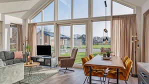 Ein geräumiges Wohnzimmer mit großem Fenster, einem Flachbildfernseher, einer Couch, einem Couchtisch und einem Essbereich mit Holztisch und Stühlen.