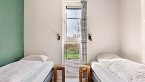 Ein Schlafzimmer mit zwei Betten, einem Fenster mit Gartenblick und einer Tür.