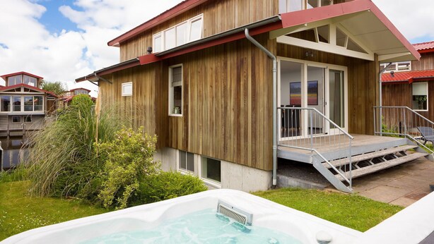 Une maison en bois avec un jacuzzi en premier plan, une véranda et un escalier menant à une porte.