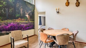 Un comedor con una mesa redonda de madera, seis sillas tapizadas y un mural grande con motivos forestales.