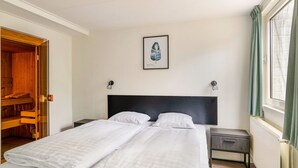 Habitación de hotel con cama doble, mesita de noche, una lámpara de noche, un cuadro en la pared y una ventana con cortinas.