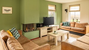 A living room with a fireplace, a television, a sofa, and a coffee table. - Bungalow Wellness 16 (Vlagtwedde)