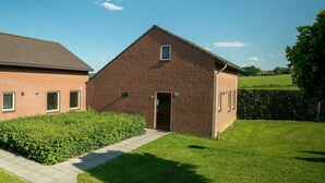 Een bakstenen gebouw met een rode deur en een klein raam, omgeven door een verzorgd gazon en een haag.