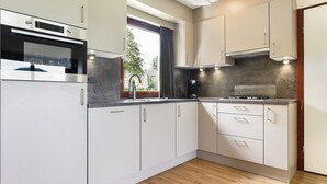 Een moderne keuken met witte kastjes, een inbouwoven, een gasfornuis en een raam met uitzicht op groen.