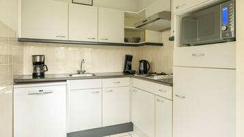 Een koelkast, een kookplaat, een koffiezetapparaat/waterkoker, eettafels