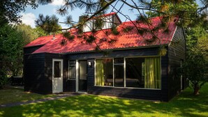A two-story wooden house with a red roof, large windows, and a door.