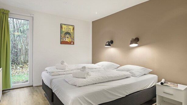 A bedroom with a bed, two bedside lamps, a nightstand, and a window with curtains.