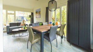 Een moderne woonkamer met een eethoek, grote ramen en uitzicht op groen.