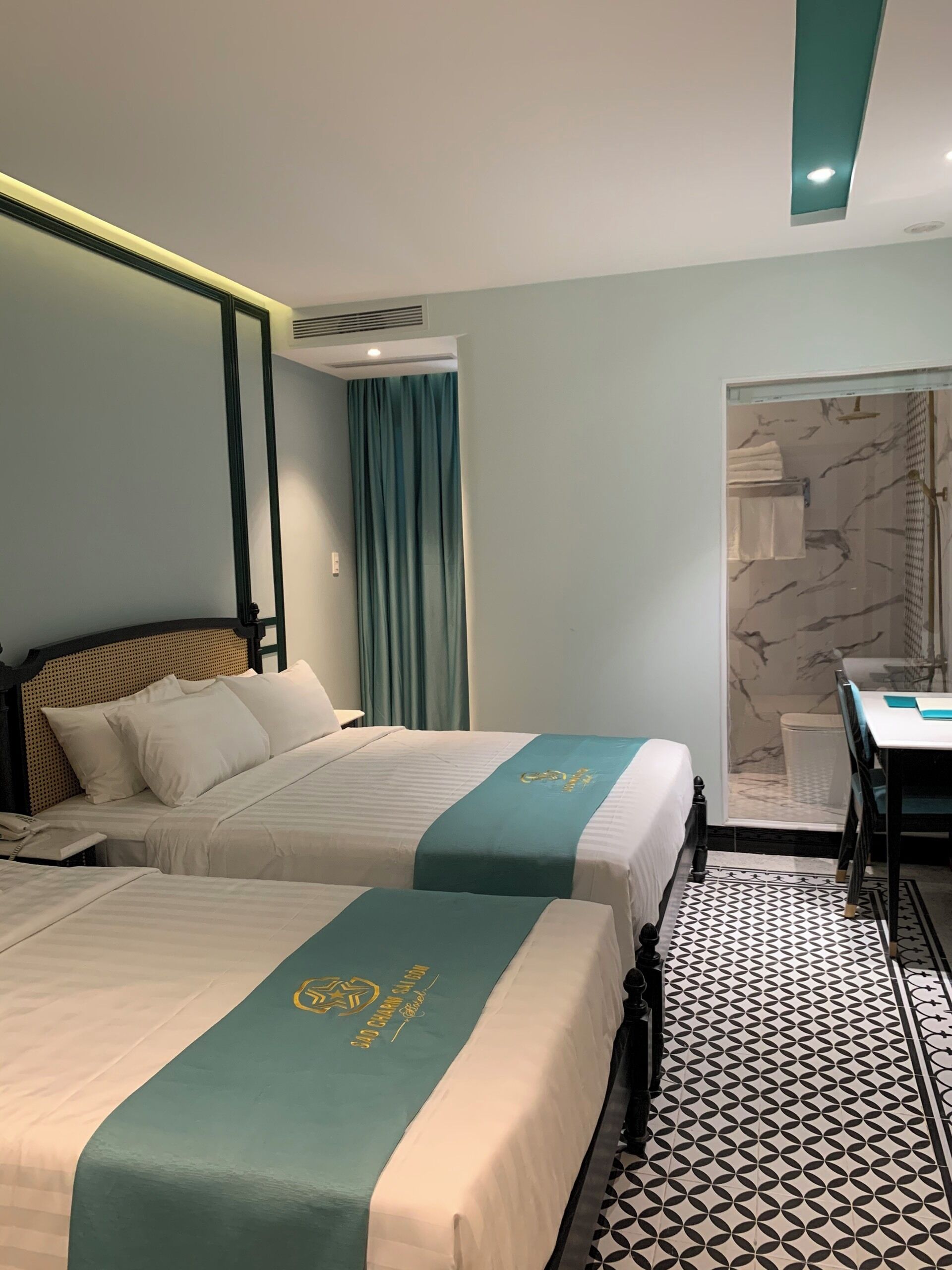 A hotel room with two beds, a desk, and a shower area.