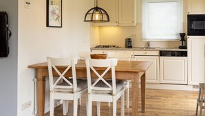 Une cuisine avec une table en bois, des chaises blanches, un luminaire suspendu et des armoires blanches.