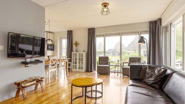 Un salon moderne avec un canapé en cuir, une table basse en bois et un téléviseur fixé au mur.