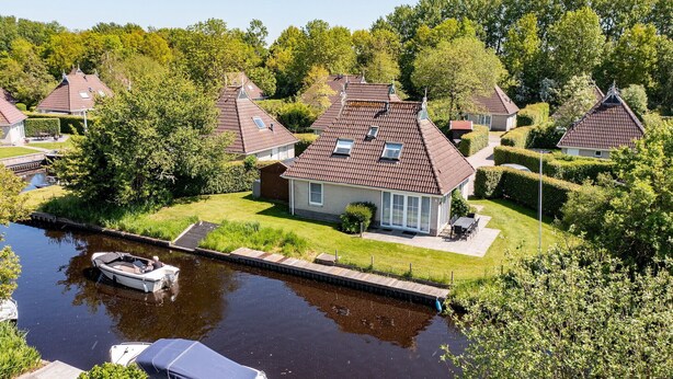 A residential area with houses, a canal, and a boat docked near the water. - Detached bungalow for 8 persons (Eernewoude)