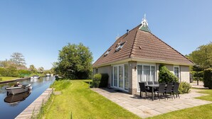 A house with a tiled roof, a small garden, and a canal with boats. - Detached bungalow for 8 persons (Eernewoude)