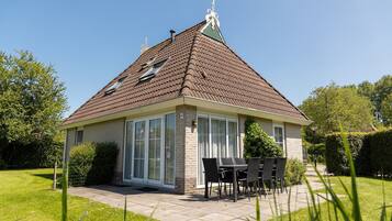 Een huis met een pannendak, grote ramen en een terras met tuinmeubilair.