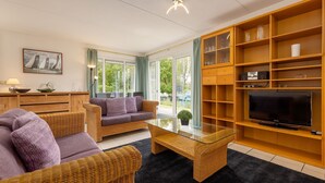 A modern living room with wicker furniture, a glass coffee table, and a TV on a wooden shelf. - Detached bungalow for 8 persons (Eernewoude)
